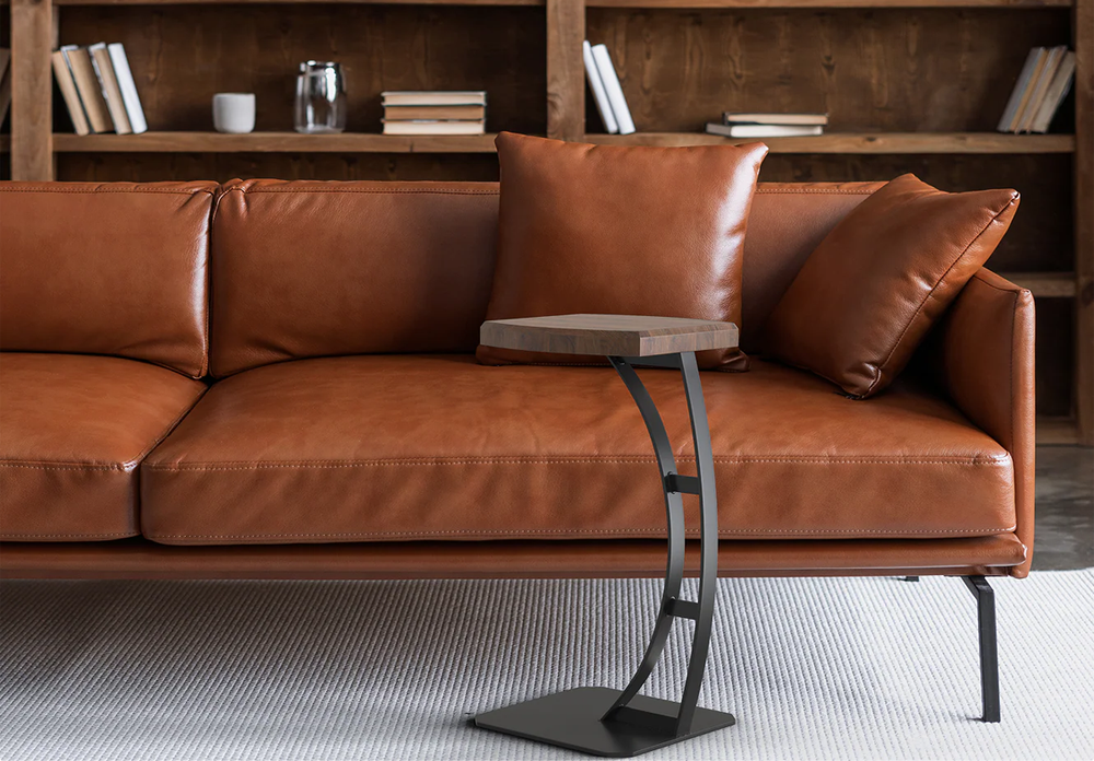 Fig & Forge bespoke cantilever C-table with a walnut top positioned over a luxurious tan leather sofa, showcasing the heavy-duty steel base and functional proximity