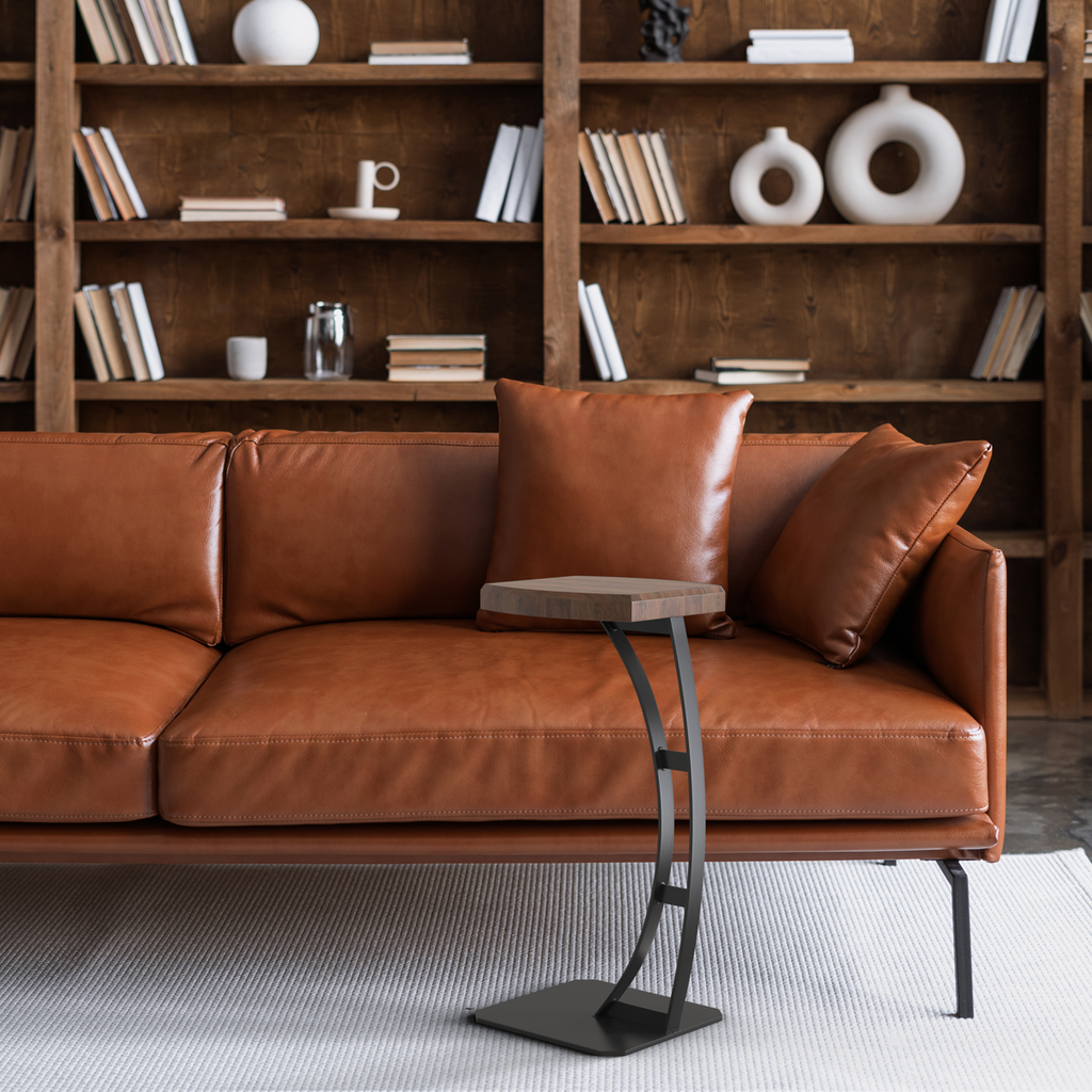 Fig & Forge bespoke cantilever C-table with a walnut top positioned over a luxurious tan leather sofa, showcasing the heavy-duty steel base and functional proximity